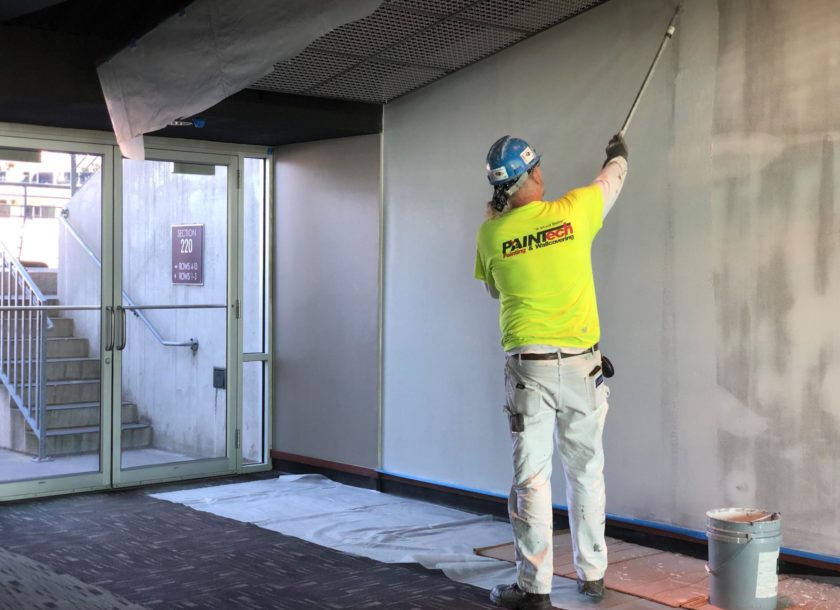 PAINTech emlpoyee painting a white wall inside a stadium