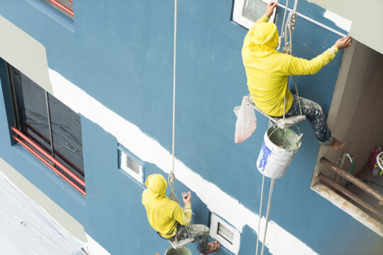 Two contractors painting a building's exterior