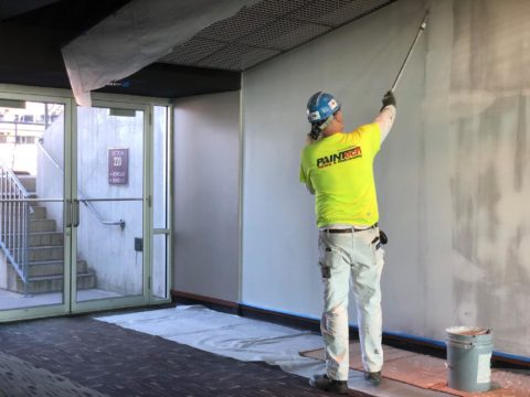 PAINTech emlpoyee painting a white wall inside a stadium